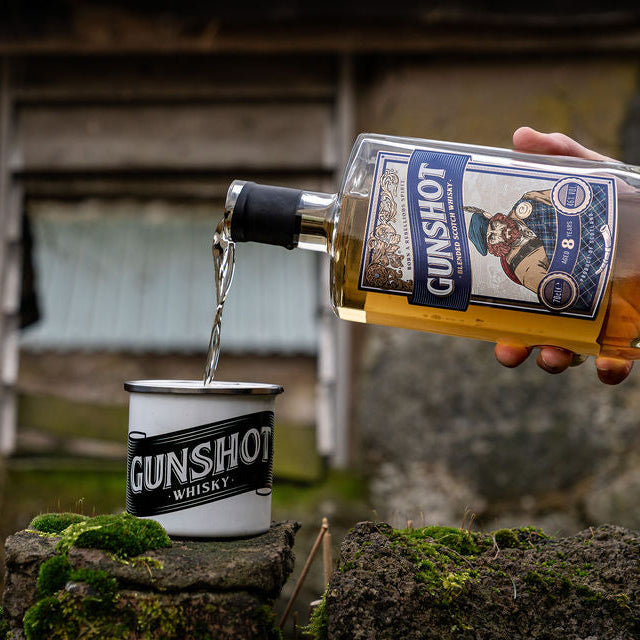 Person pouring Gunshot Whisky into a metal cup with a rustic background