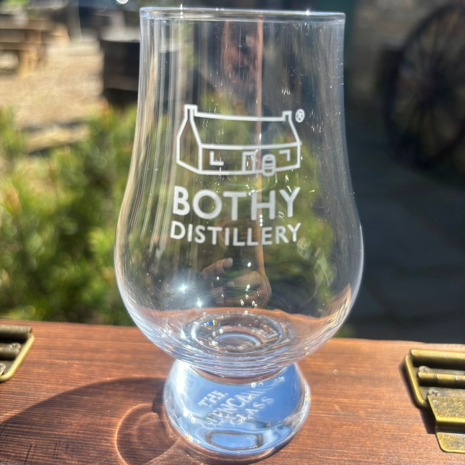 Clear Glencairn glass with engraved text on a wooden surface, blurred background