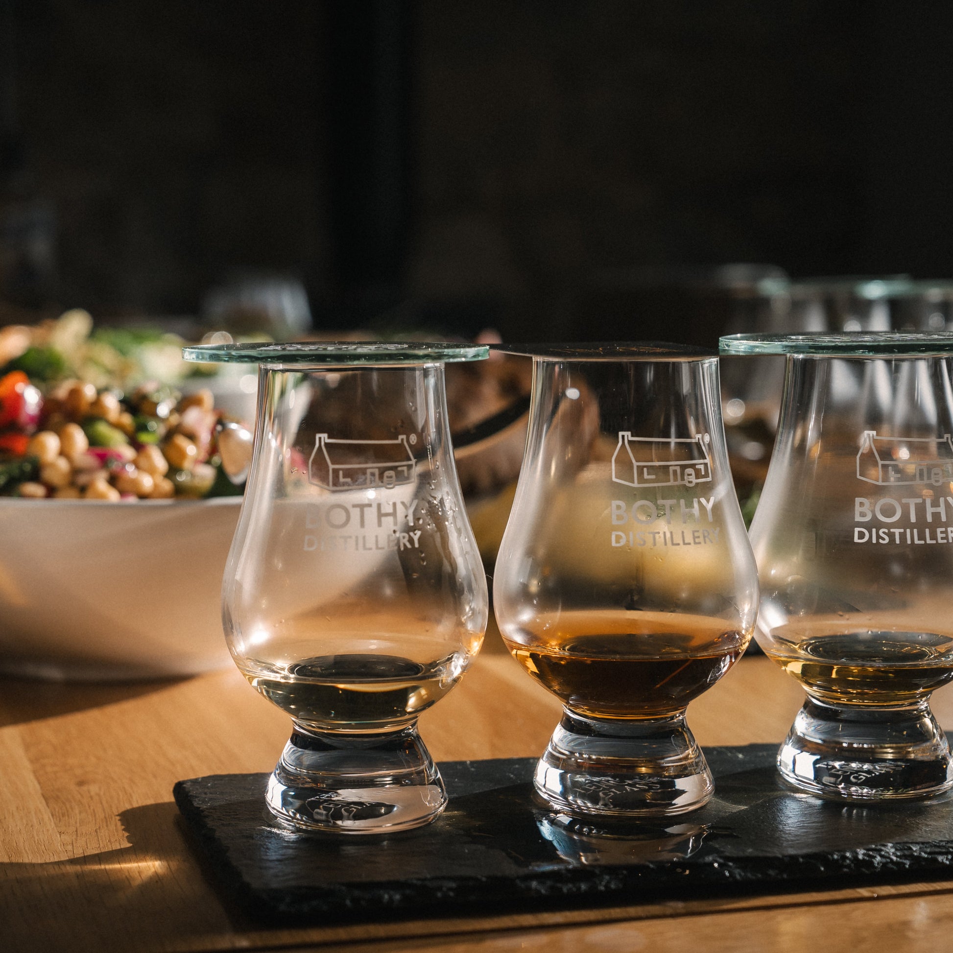 Bottle of Bothy Distillery whisky with three glasses on a wooden surface.