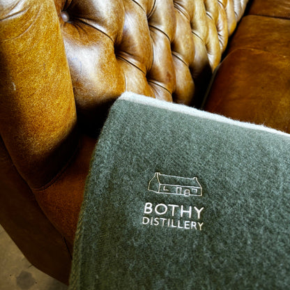 Brown leather cushion with a gray blanket featuring 'Botthy Distillery' text.