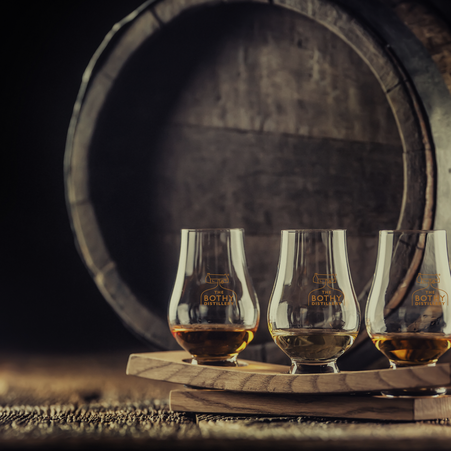Three glasses of whiskey on a wooden tray with a barrel in the background