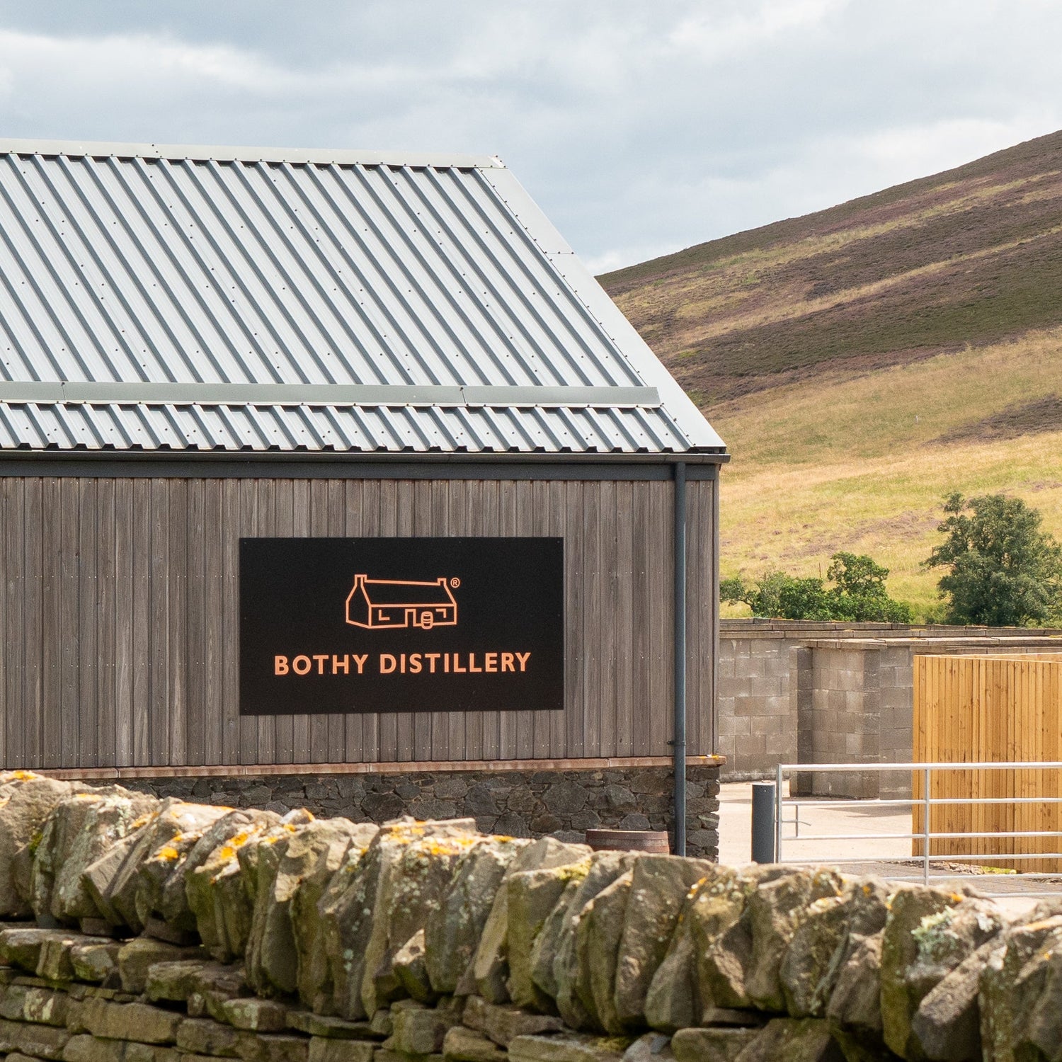 Wooden building with 'Bothy Distillery' sign in a scenic outdoor setting